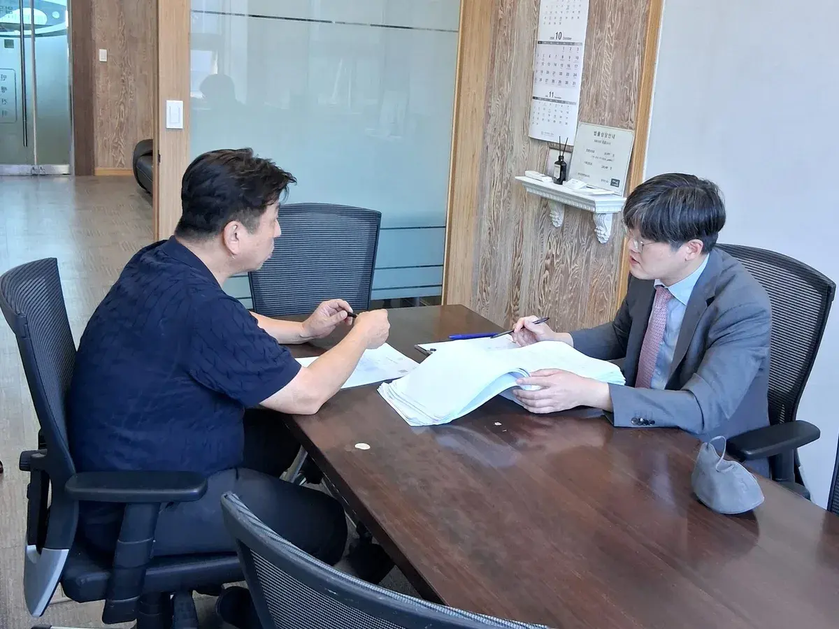 상담실에서 변호사가 의뢰인과 마주 앉아 서류를 함께 보며 이야기하는 모습