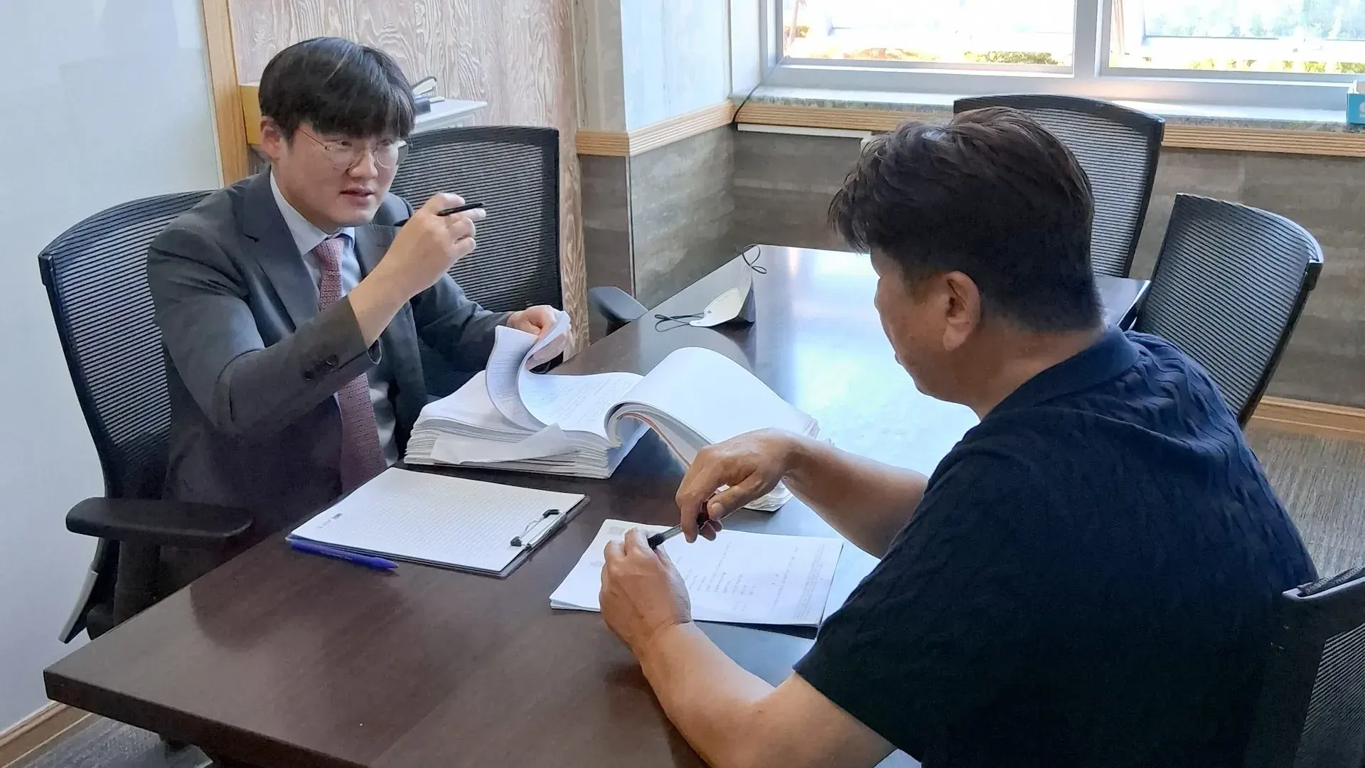 변호사가 책상에서 의뢰인에게 서류를 짚어 가며 설명하는 모습